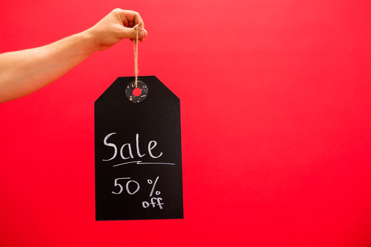 Hand holding a black sale tag with 50% off on a vibrant red background.